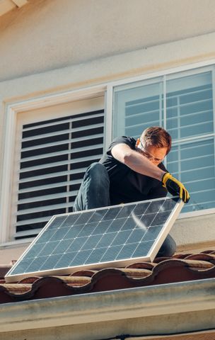 Technician carrying a solar panel on a roof